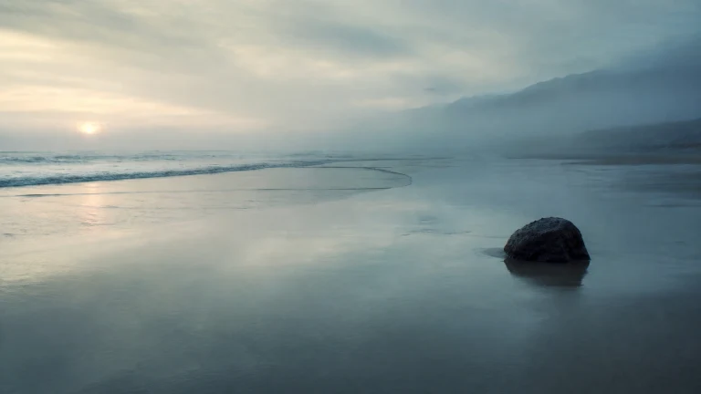 灰蓝海滩退潮水面映着晨光，浅水中露出一块圆石