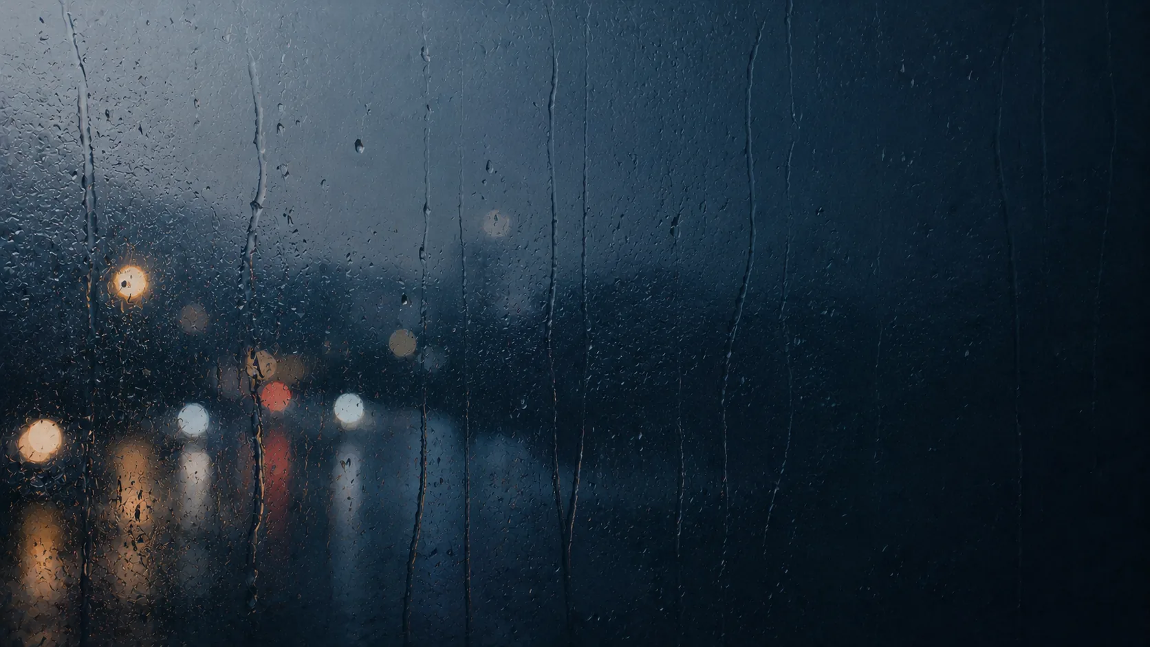 雨水沿深色窗玻璃流下，窗外街灯化成朦胧光点